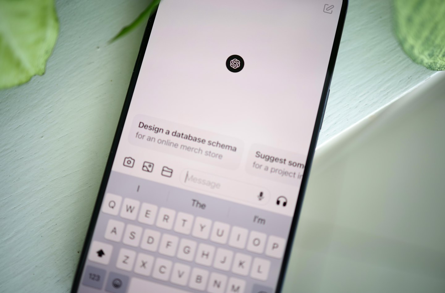 Teléfono inteligente mostrando indicaciones de chatbot y teclado virtual sobre un escritorio.