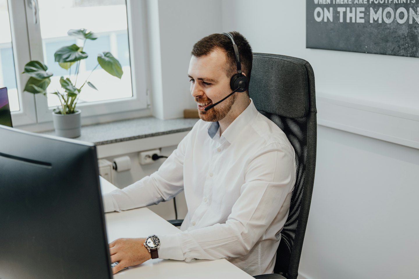 Hombre con auriculares sonríe mientras trabaja en una computadora.